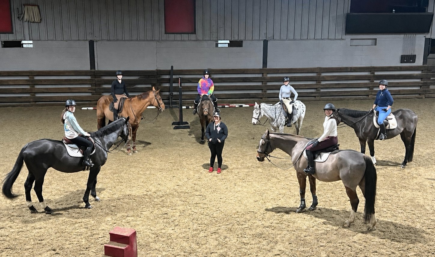 Children riding horses in an indoor arena with instructors at Lionheart Stables