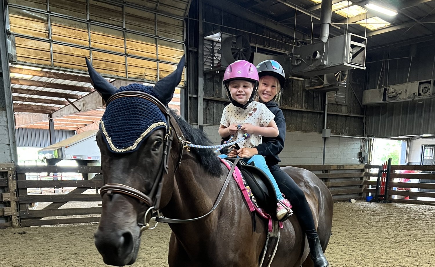 Two children riding a black horse in a barn at Lionheart Stables